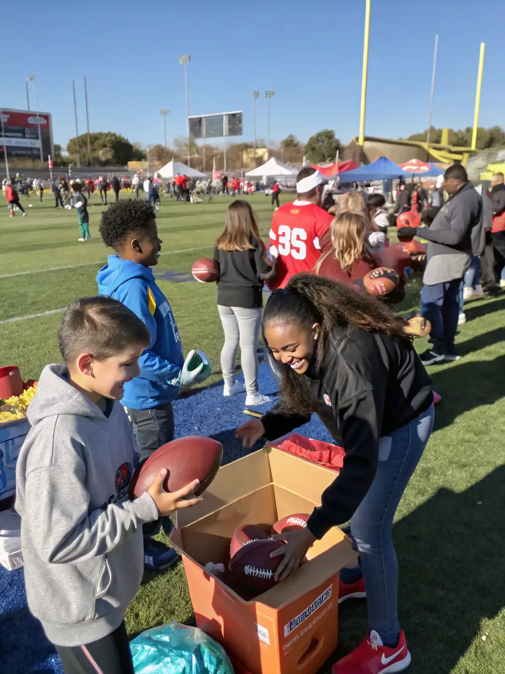 A group of volunteers assisting young athletes with football drills on a sunny field, showcasing teamwork and mentorship.